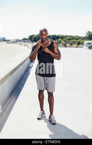 Full length portrait of fit young man outside listening to music on earphones. Muscular young male model. Stock Photo