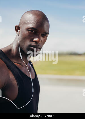 Image of handsome young man wearing earphones looking at camera. African male model outdoors. Stock Photo
