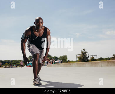 Fit young man on his mark to start running. Determined athlete outdoors. Muscular African male model ready for his run on a hot Stock Photo