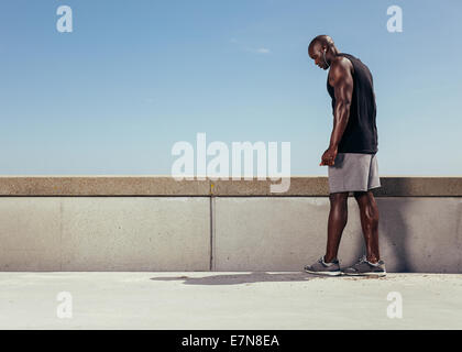 Image muscular young man on a walkway getting ready for his run. Focused male athlete preparing for his running workout outdoors Stock Photo