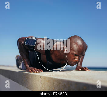 Image of sporty man doing push-ups. Strong young fitness model exercising. African male model workout outdoors. Stock Photo