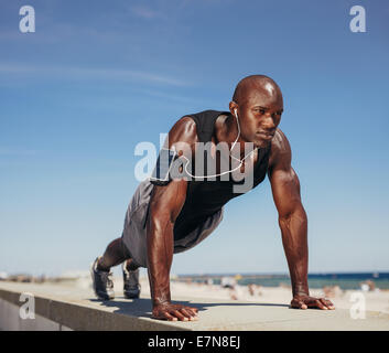 Muscular man doing push ups against blue sky. Strong male athlete working out outdoors. Stock Photo