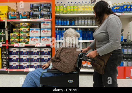 An elderly woman in a wheelchair and her carer or assistant looking at drinks in a supermarket. Stock Photo