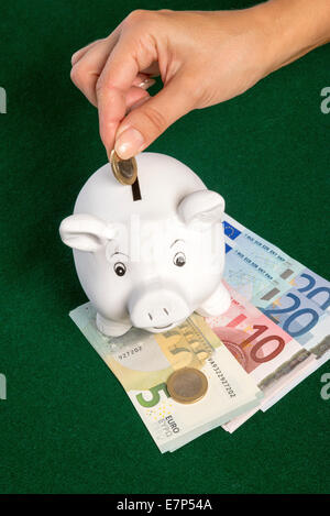 Euros and a piggy bank money box Coin being placed into moneybox slot Stock Photo