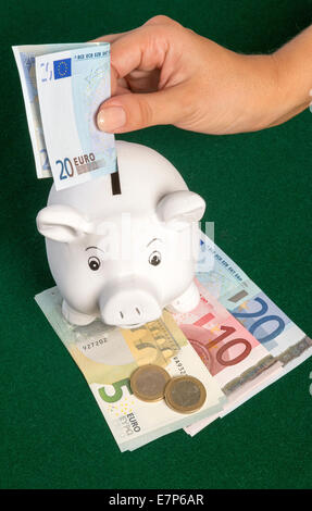 Euros and a piggy bank money box A twenty Euro banknote being placed into slot Stock Photo