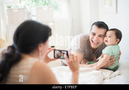 Mother photographing father with baby son (6-11 months) in bedroom Stock Photo