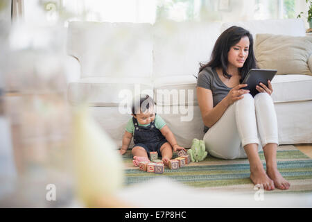 Mother using tablet pc while her son (6-11 months) playing with building blocks Stock Photo