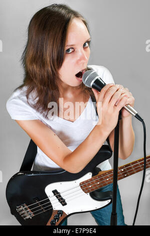 Girl with bass guitar and microphone isolated on gray background Stock Photo