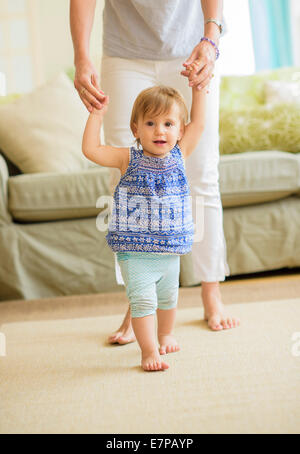 Mother assisting baby daughter (18-23 months) with her first steps Stock Photo