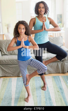 Mother and daughter (8-9) doing in yoga poses in living room Stock Photo