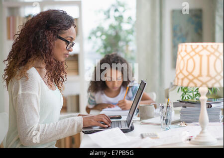 Woman using laptop at home, girl (8-9) doing homework in background Stock Photo