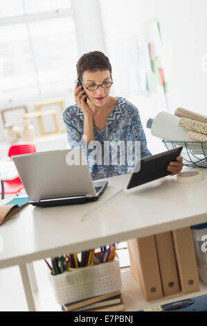 Senior business woman using cell phone and tablet pc in office Stock Photo