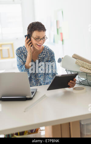 Senior business woman using cell phone and tablet pc in office Stock Photo