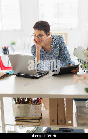 Senior business woman using cell phone and tablet pc in office Stock Photo