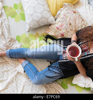 Woman lying down on bed with tea cup Stock Photo