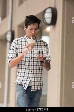 Man walking on sidewalk with iced coffee and mobile phone Stock Photo