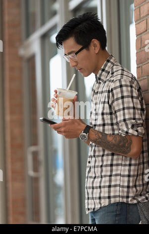 Man walking on sidewalk with iced coffee and mobile phone Stock Photo