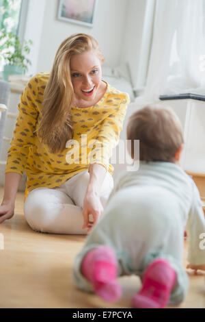 Mother looking at baby daughter (6-11 months) crawling Stock Photo