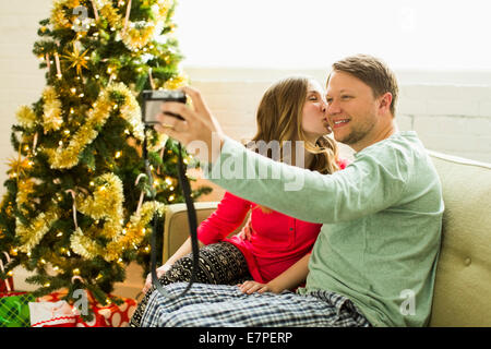 Young couple taking selfie on sofa at Christmas Stock Photo