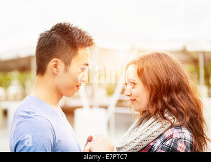 Romantic interracial young couple holding hands and looking at each other outside in sunset light Stock Photo