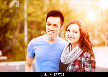 Romantic interracial young couple standing together and looking at camera outside in sunset light Stock Photo