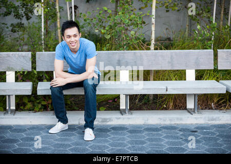 Young asian man sitting and smiling on park bench with copy space Stock Photo