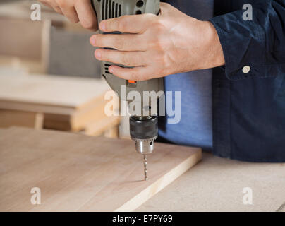 Carpenter Using Drill On Wood In Workshop Stock Photo