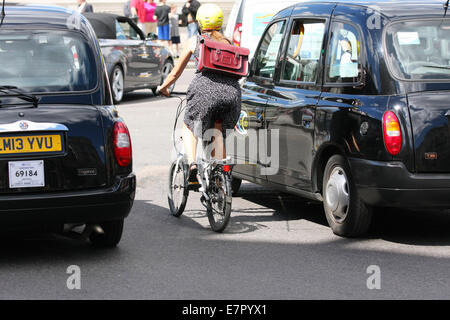 Rear view of a female riding a folding cycle between two taxis in Trafalgar Square, London Stock Photo