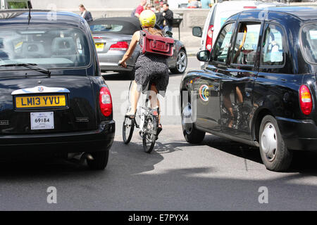 Rear view of a female riding a folding cycle between two taxis in Trafalgar Square, London Stock Photo