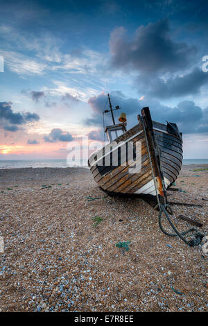 Beautiful sunrise over an old wooden fishing boat on a shingle beach