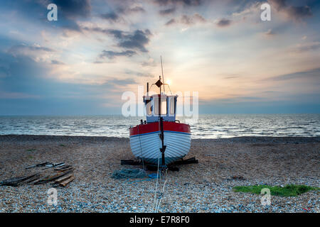 Red and white wooden fishing boat on a shingle beach Stock Photo