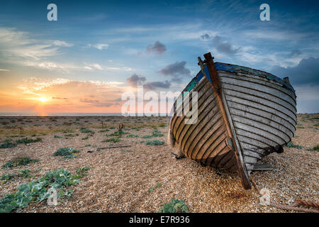 A beautiful sunrise over a wooden fishing boat on s shingle beach Stock Photo