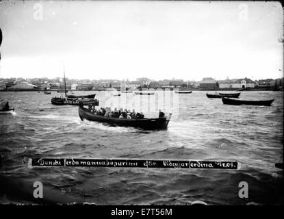 A photograph from 1909 showing a Danish tourist group in the Reykjavik harbor. The image captures the travel group and the boats typical for the era, reflecting Icelandic tourism during the early 20th century. Stock Photo