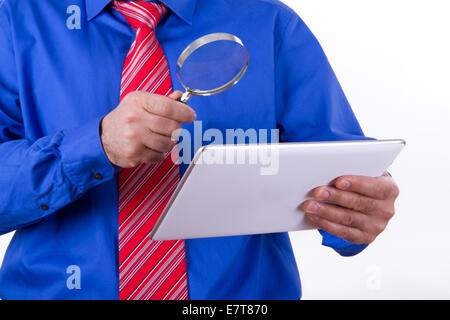 Businessman with red tie and blue shirt holding magnifying glass to tablet, isolated on white background. Stock Photo