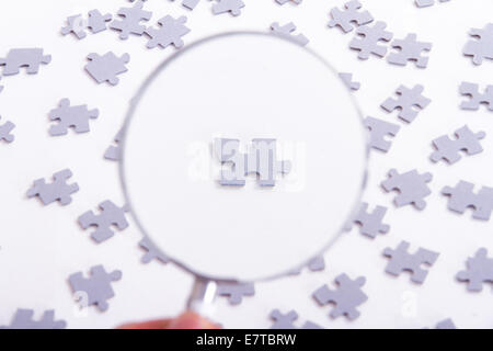 Hand holding classic style magnifying glass and examining single little puzzle piece among others on white. Stock Photo