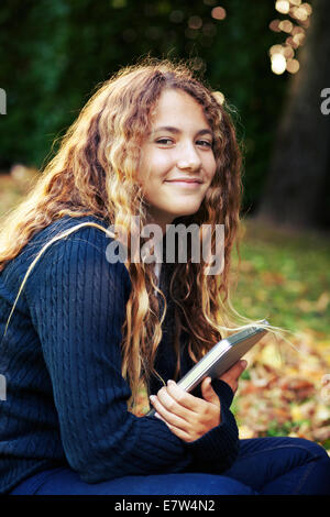 Teenager female girl student with laptop outdoor in the garden with fallen leaves. Autumn Stock Photo