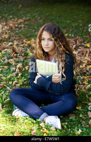 Teenager female girl student with laptop outdoor in the garden with fallen leaves. Autumn Stock Photo