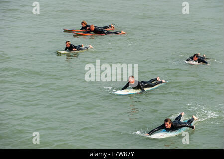 Group of surfers in wetsuits lying flat on their surfboards in the sea, paddling out towards the waves Stock Photo