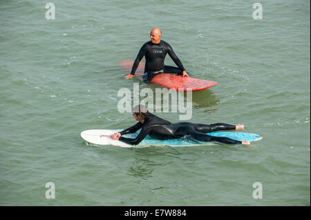 Two surfers in wetsuits waiting on their surfboards for a big wave / breaker to surf on along the North Sea coast Stock Photo