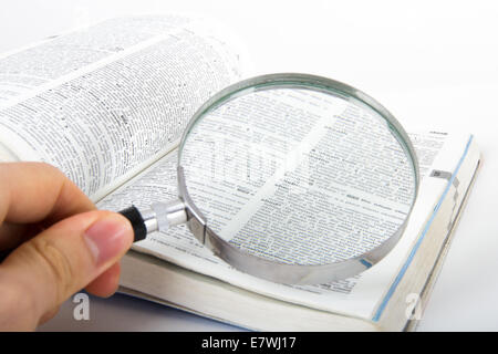 Hand holding classic style magnifying glass, searching for a word on open dictionary book, isolated on white background. Stock Photo