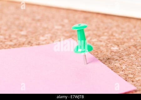 Green push pin and pink sticky post on cork bulletin board. Stock Photo
