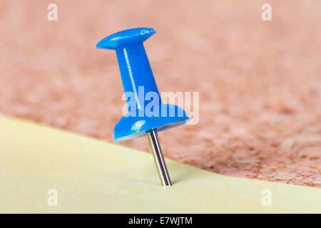Macro view of blue push pin on yellow sticky post it note on cork bulletin board. Stock Photo