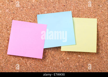 Blank, empty, multi colored sticky post it notes for your messages, pink, blue and yellow on cork bulletin board. Stock Photo