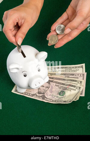 US Dollars and a piggy bank with woman's hand placing coins into the white pig Stock Photo