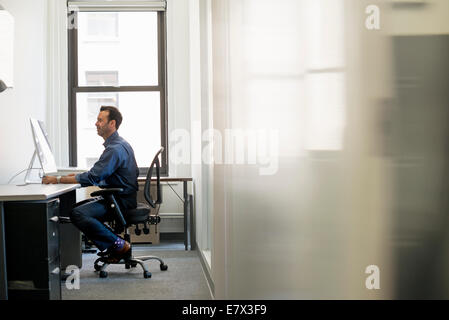 Office life. A man in casual clothing seated at a desk looking at a computer screen. Stock Photo