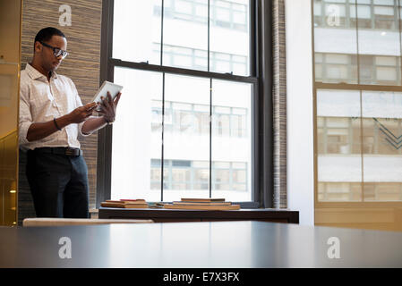 A man standing by a window in an office using a digital tablet. Stock Photo