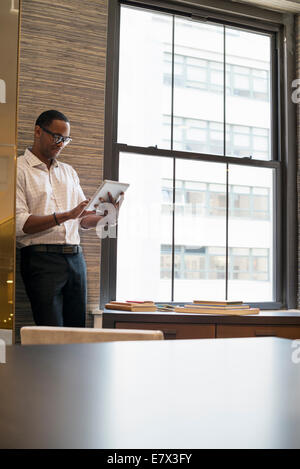 A man standing by a window in an office using a digital tablet. Stock Photo