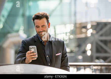 A man seated on a bench checking his smart phone. Stock Photo