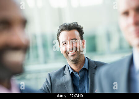 Three businessmen, one smiling at the camera, looking between two others. Stock Photo