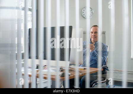 View through an office partition of a man seated at a desk. Stock Photo
